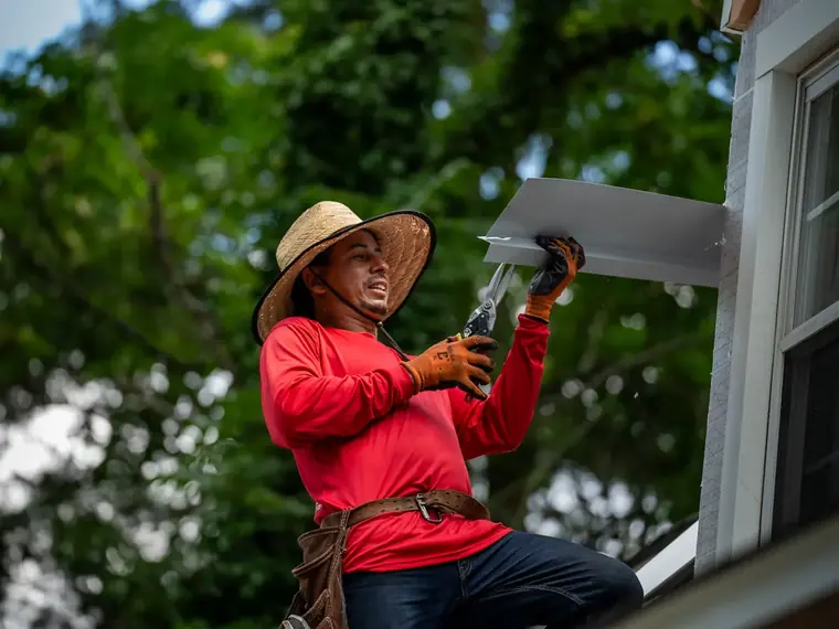 An A&J crew member holding a length of newly formed seamless gutter on site